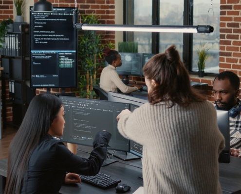 Two workers looking at code on computer monitor